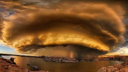 A wide, layered arc of cloud advancing across a lake at sunset
