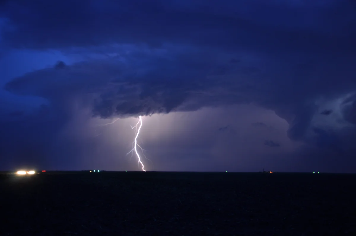 A cloud-to-ground lightning strike beneath a supercell at dusk, seen across open plains